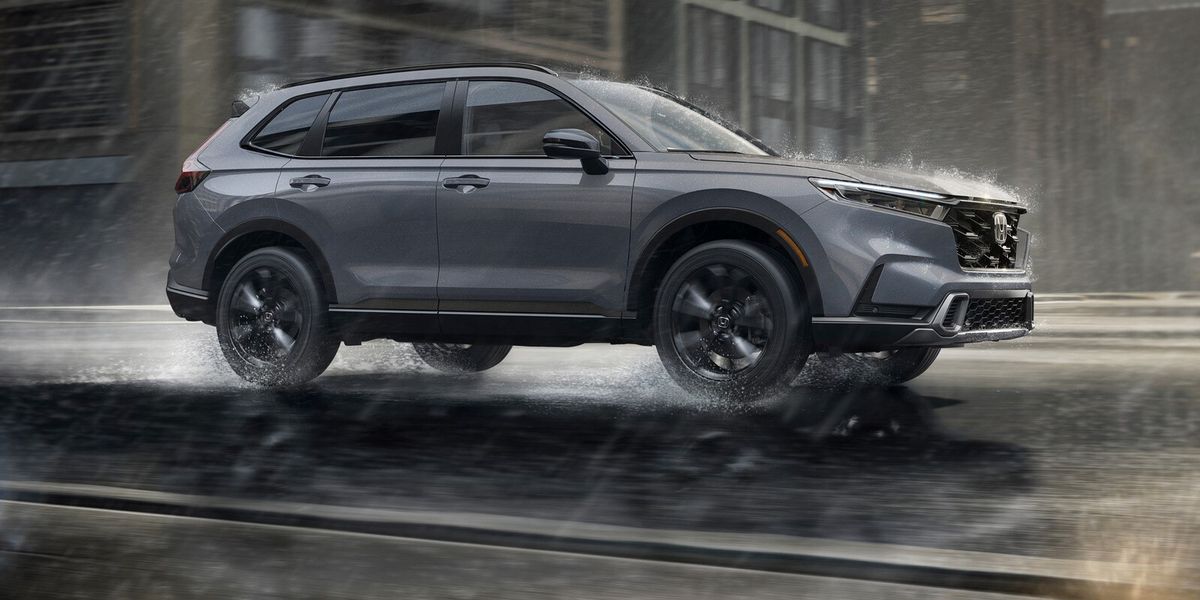 2027 Honda CR-V Sport Touring Hybrid in Urban Gray Pearl profile driving on a rainy city street (Compact Crossover SUV).