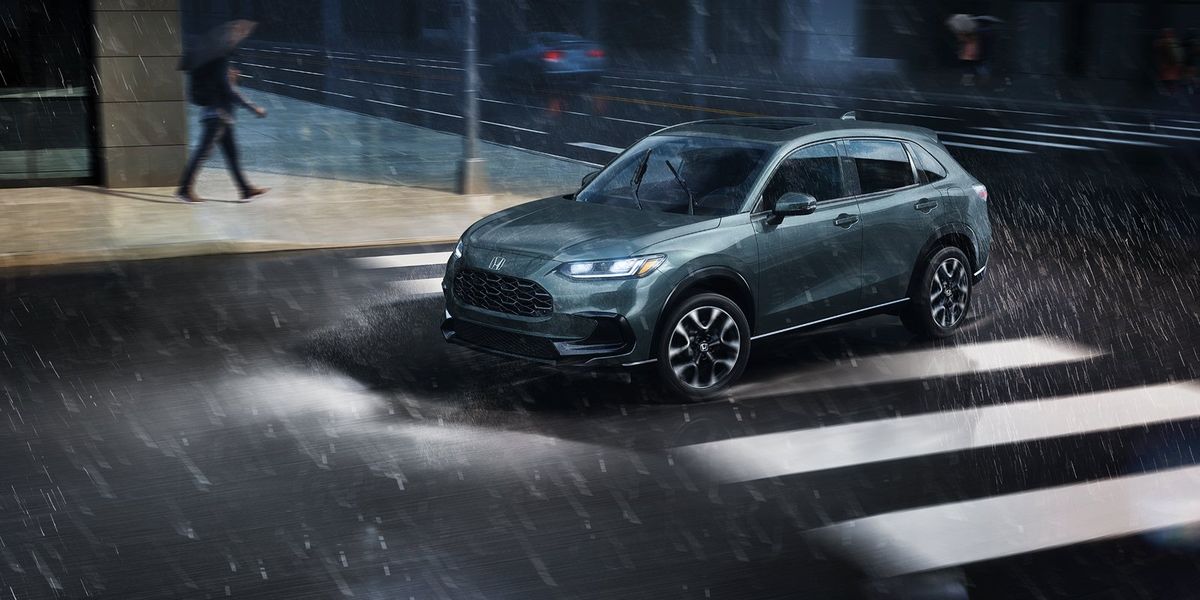 2027 Honda HR-V EX-L in Nordic Forest Pearl profile view driving on a rainy city street (Subcompact Crossover SUV).